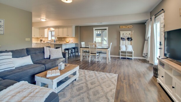 A spacious living room with a gray sofa, a wooden coffee table, and a patterned rug. A dining area with a white table and chairs is visible in the background. - Waterfront Home Near Mark Twain National Forest (Poplar Bluff)
