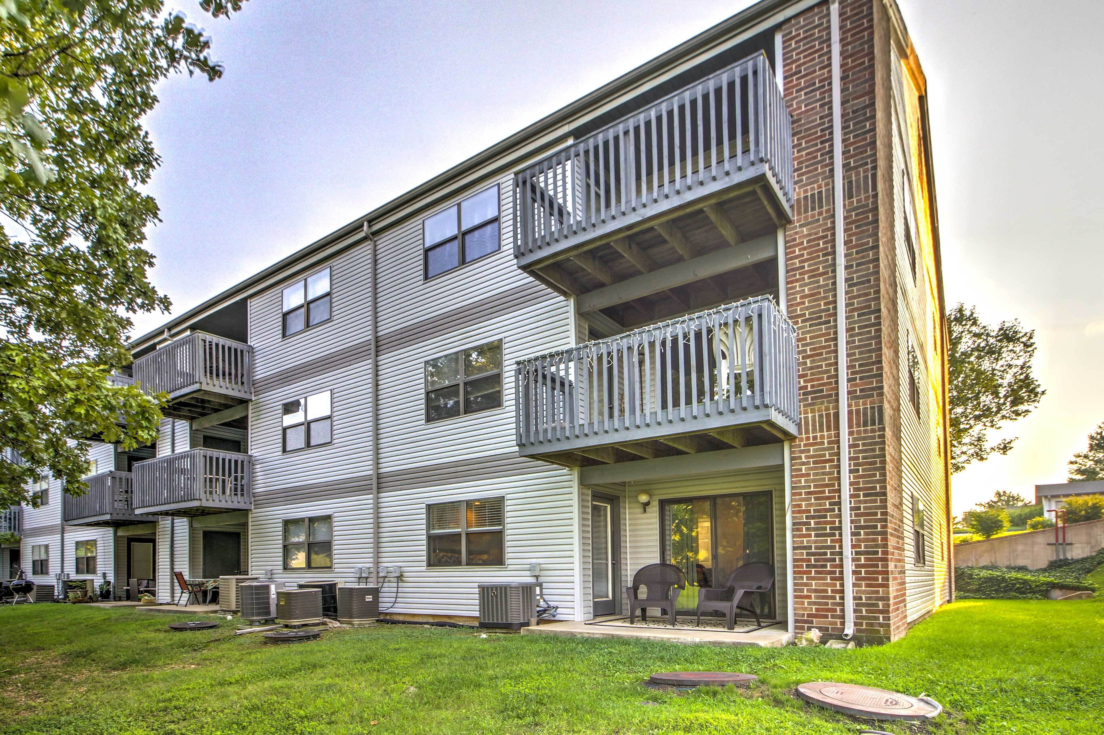 A multi-story apartment building with balconies, a covered patio, and a grassy yard.