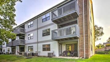 A multi-story apartment building with balconies, a covered patio, and a grassy yard.