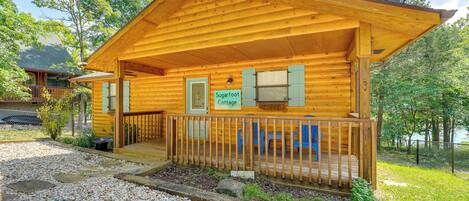 Una cabaña de madera con un porche, un cartel que dice "Sugarfoot Cottage" y una antena parabólica en el techo.
