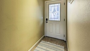 A hallway with a white door featuring a stained glass window, a textured beige wall, and a patterned rug on the floor. - Cozy Table Rock Lake Vacation Rental w/ Deck (Golden)