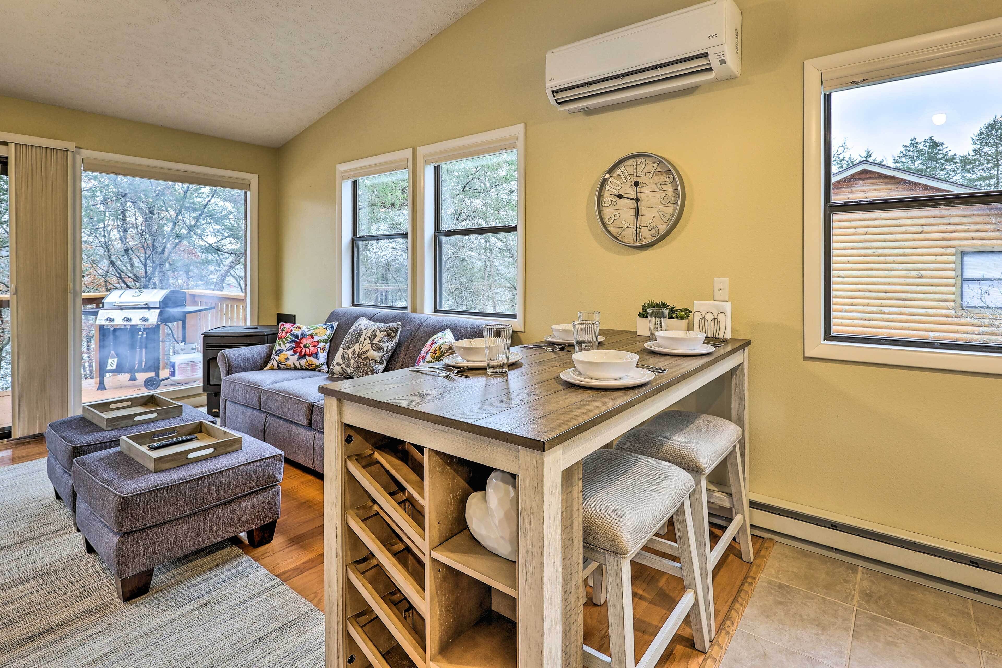 A cozy living room with a sofa, ottomans, a wooden coffee table, and a dining area with a clock on the wall.