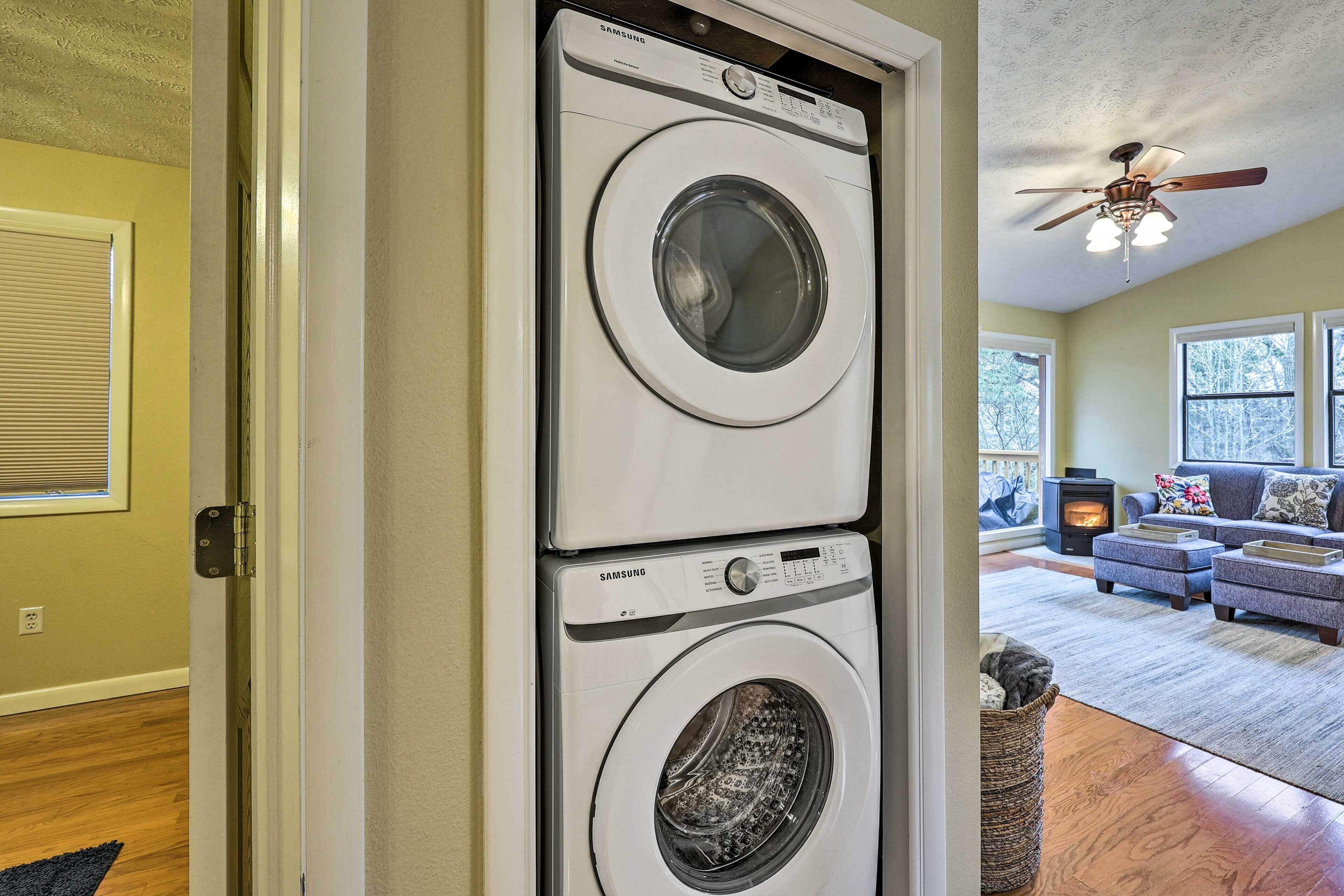 A laundry room with two stacked front-loading washers and dryers, a ceiling fan, and a living area with a sofa and a fireplace.