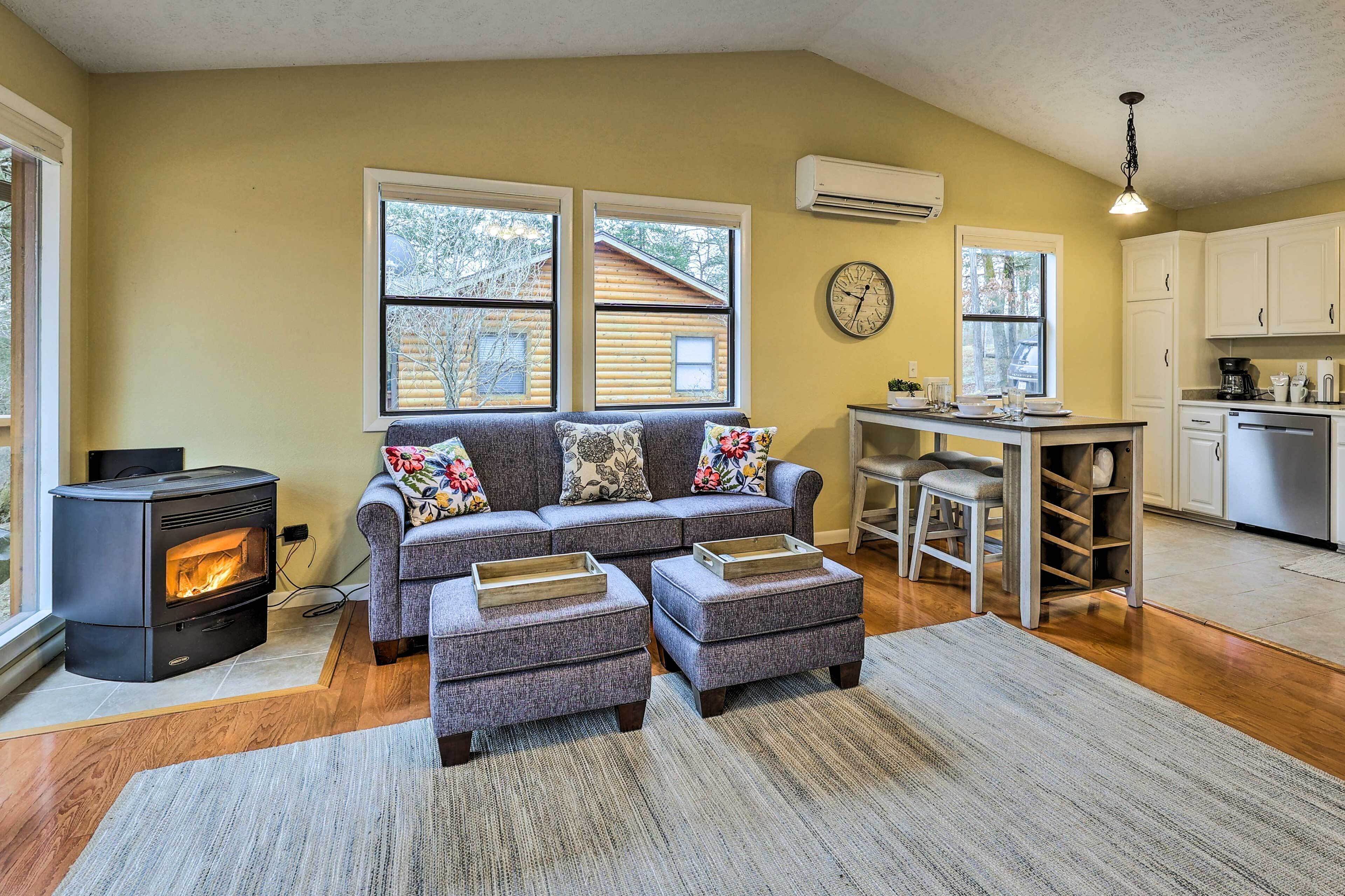 A cozy living room with a sofa, ottomans, a fireplace, and a kitchen area.