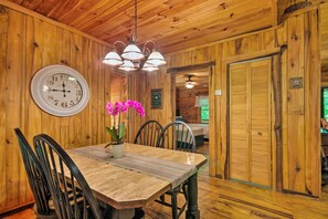 A wooden interior with a dining table, chairs, a clock, and a potted orchid.