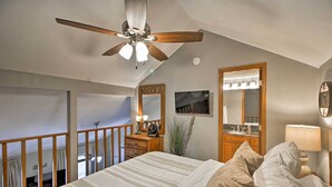 Une chambre à coucher comprenant un lit, un ventilateur de plafond, une table de chevet avec une lampe, un miroir et une vue sur le balcon.