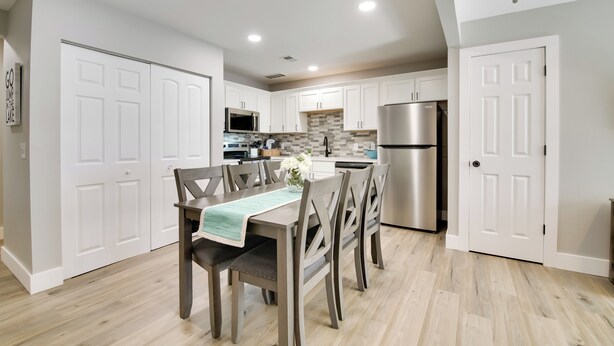 A modern kitchen with white cabinetry, stainless steel appliances, and a dining area with wooden chairs and a table. - Delightful Townhouse w/ Patio & Shared Yard! (Kimberling City)
