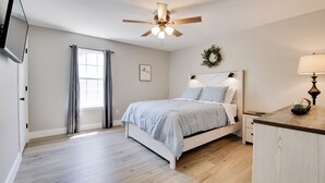 A bedroom with a bed, a ceiling fan, a window with curtains, a wall-mounted TV, and a bedside table with a lamp. - Delightful Townhouse w/ Patio & Shared Yard! (Kimberling City)