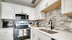 A modern kitchen with white cabinets, a stainless steel oven, a microwave, and a sink. - Delightful Townhouse w/ Patio & Shared Yard! (Kimberling City)