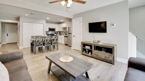 A modern kitchen with white cabinets, a dining area with a wooden table, and a living room with a sofa and a TV. - Delightful Townhouse w/ Patio & Shared Yard! (Kimberling City)