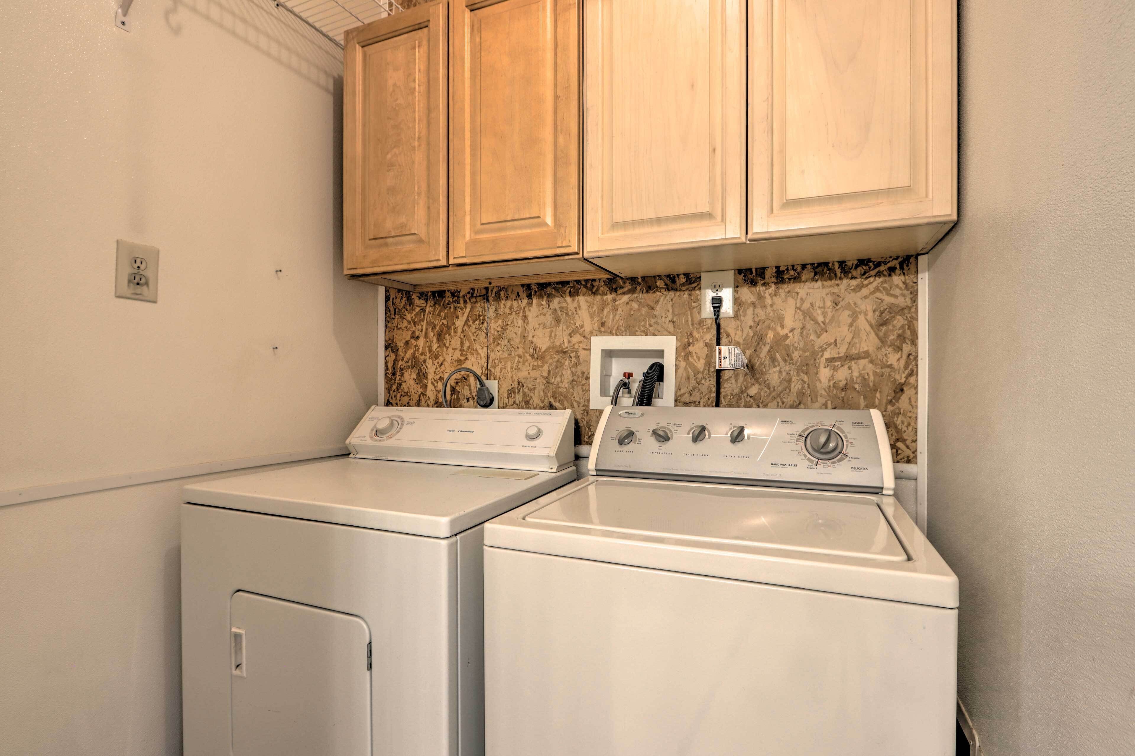 A laundry area with two washing machines and a dryer, wooden cabinets above, and a marble backsplash.