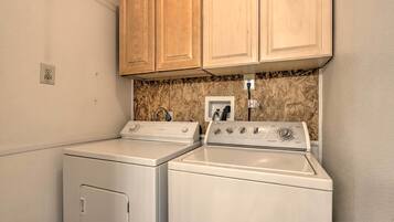A laundry area with two washing machines and a dryer, wooden cabinets above, and a marble backsplash.
