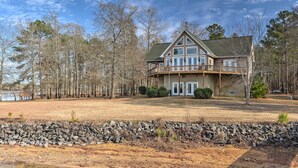 A two-story house with a balcony, surrounded by trees and a stone wall. - Dreamy Ridgeway Home w/ Grill on Lake Wateree! (Winnsboro)