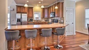 A modern kitchen with wooden cabinets, a stainless steel refrigerator, a microwave, and a large island with bar stools. - Dreamy Ridgeway Home w/ Grill on Lake Wateree! (Winnsboro)