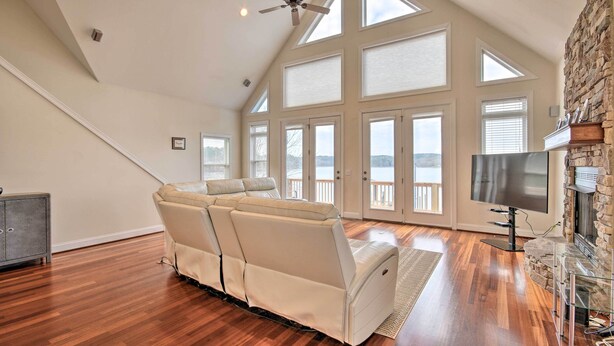 A spacious living room with a high ceiling, a ceiling fan, a large TV, and a stone fireplace. - Dreamy Ridgeway Home w/ Grill on Lake Wateree! (Winnsboro)