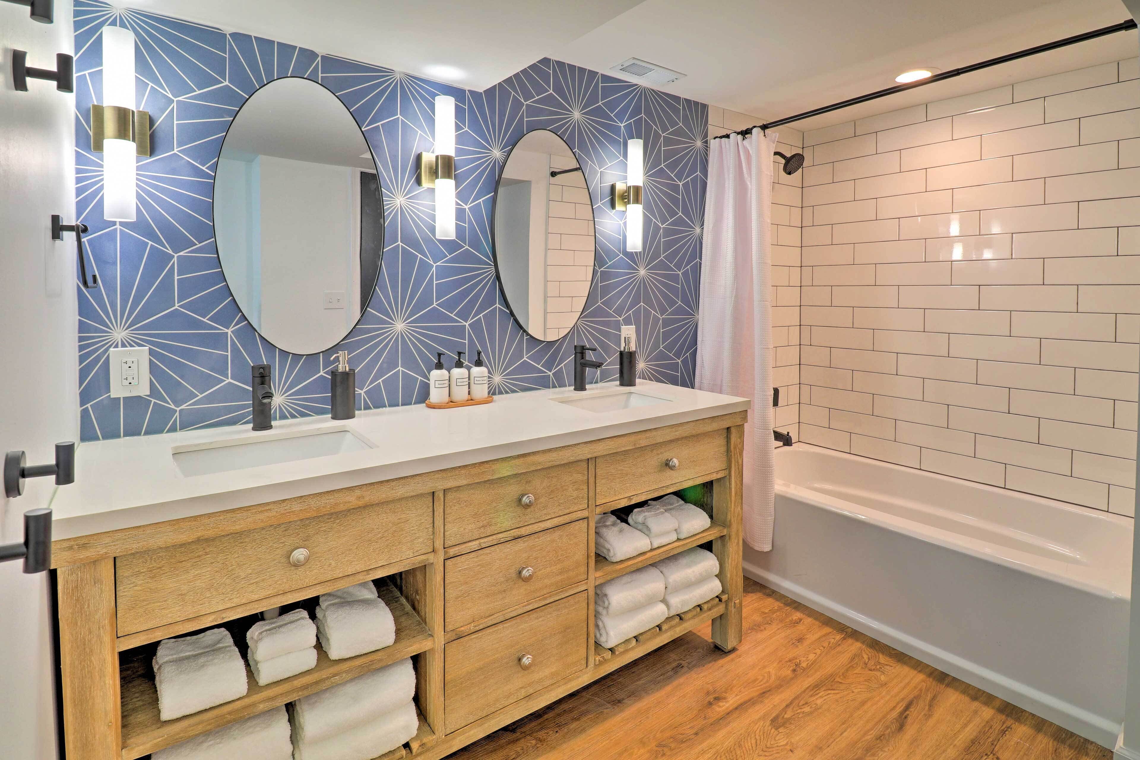 A modern bathroom with two sinks, wooden vanity, and a bathtub.