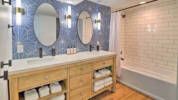 A modern bathroom with two sinks, wooden vanity, and a bathtub.