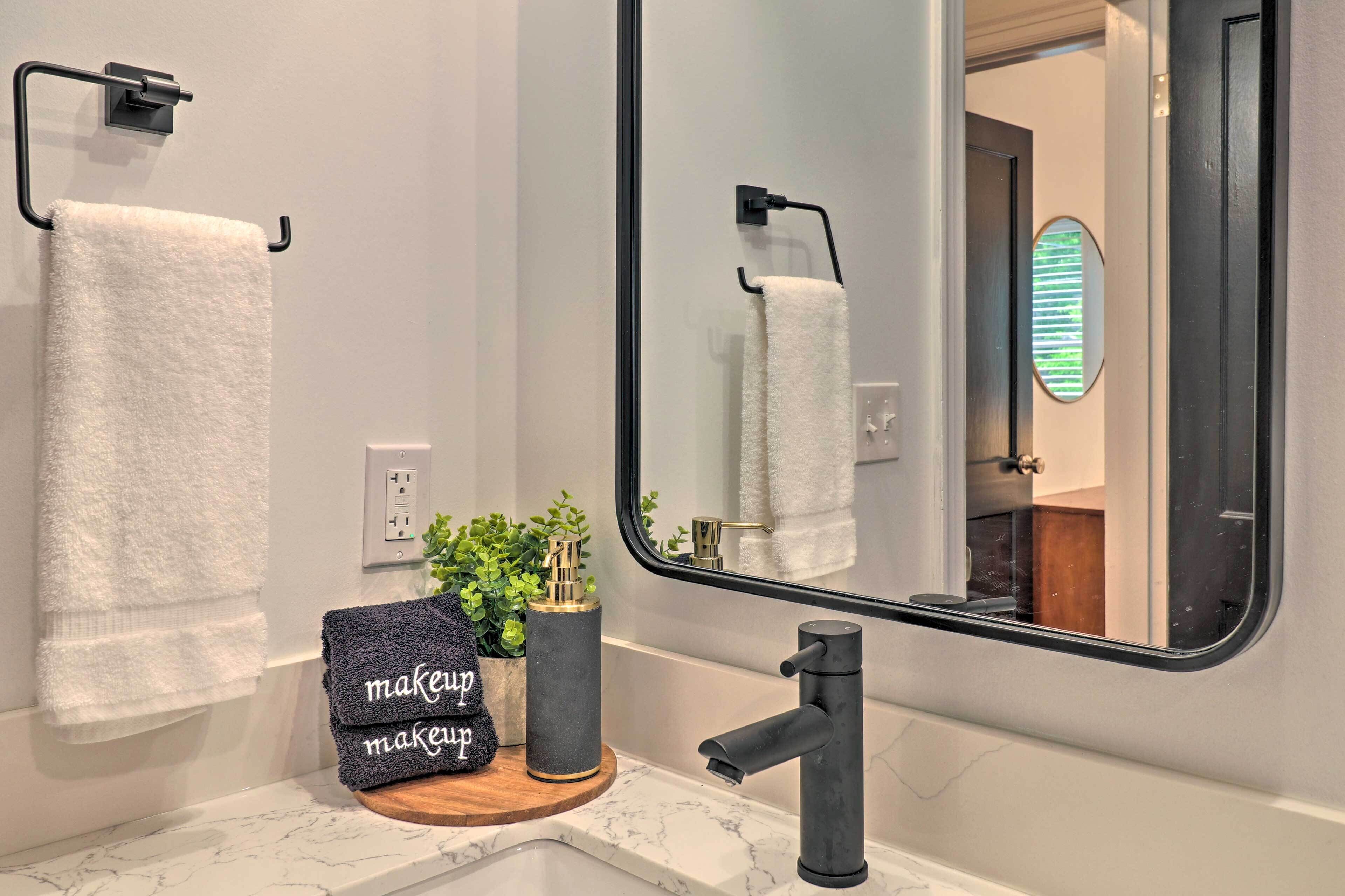 A bathroom with a white marble sink, a black faucet, a towel rack with a white towel, a small potted plant, and a mirror reflecting the bathroom.
