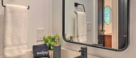 A bathroom with a white marble sink, a black faucet, a towel rack with a white towel, a small potted plant, and a mirror reflecting the bathroom.