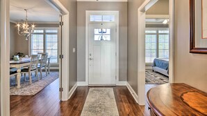 Un couloir avec un plancher en bois, une porte blanche et un lustre.