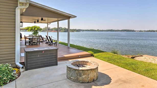 Une terrasse couverte avec un foyer en pierre, du mobilier d’extérieur et une vue sur un lac.
