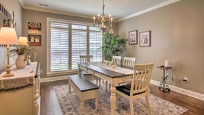 Un coin repas avec une table en bois, des chaises blanches, un banc, un lustre et une plante en pot.