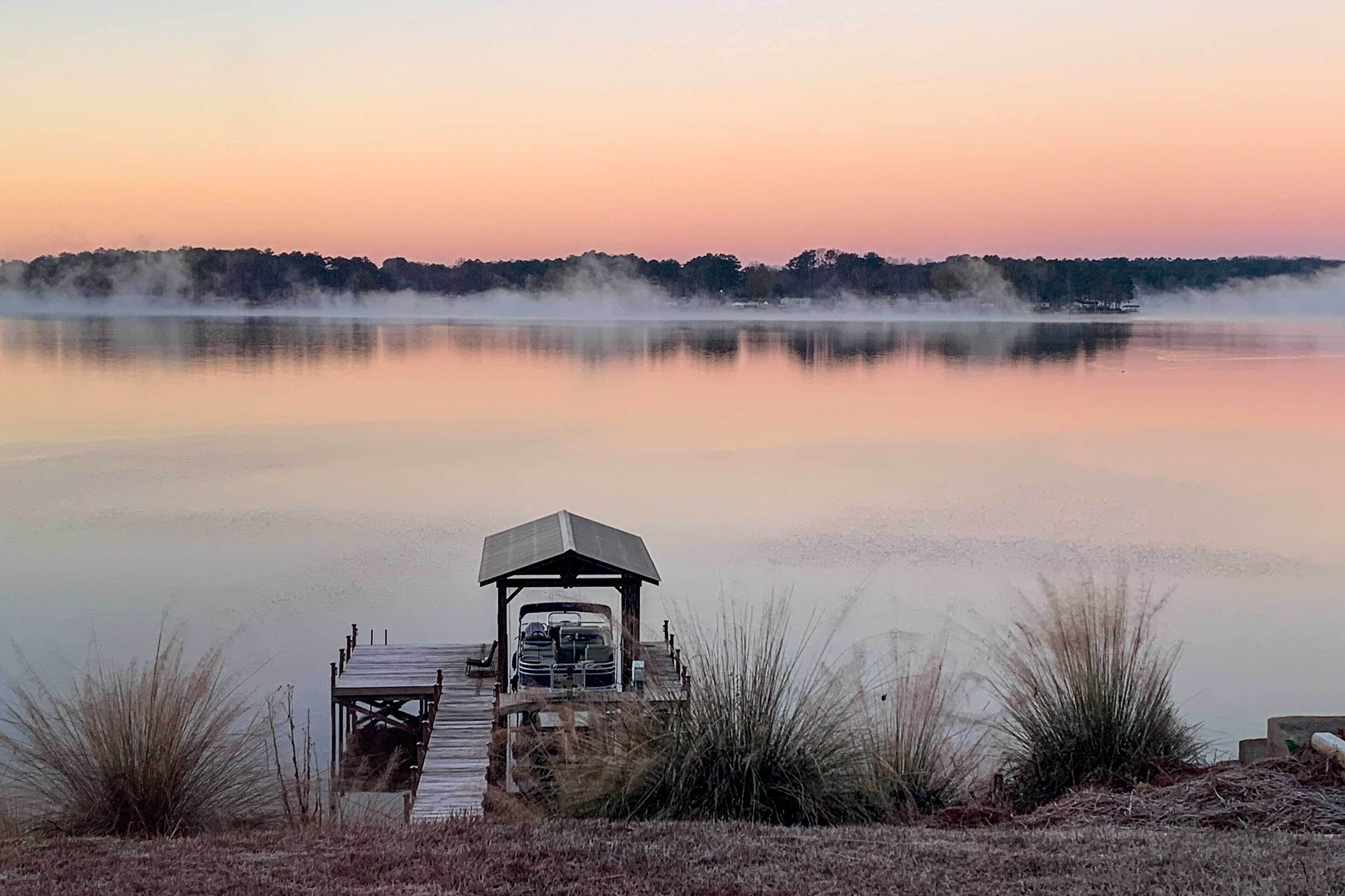 A dock leading to a gazebo by a calm lake with a misty forest in the background.
