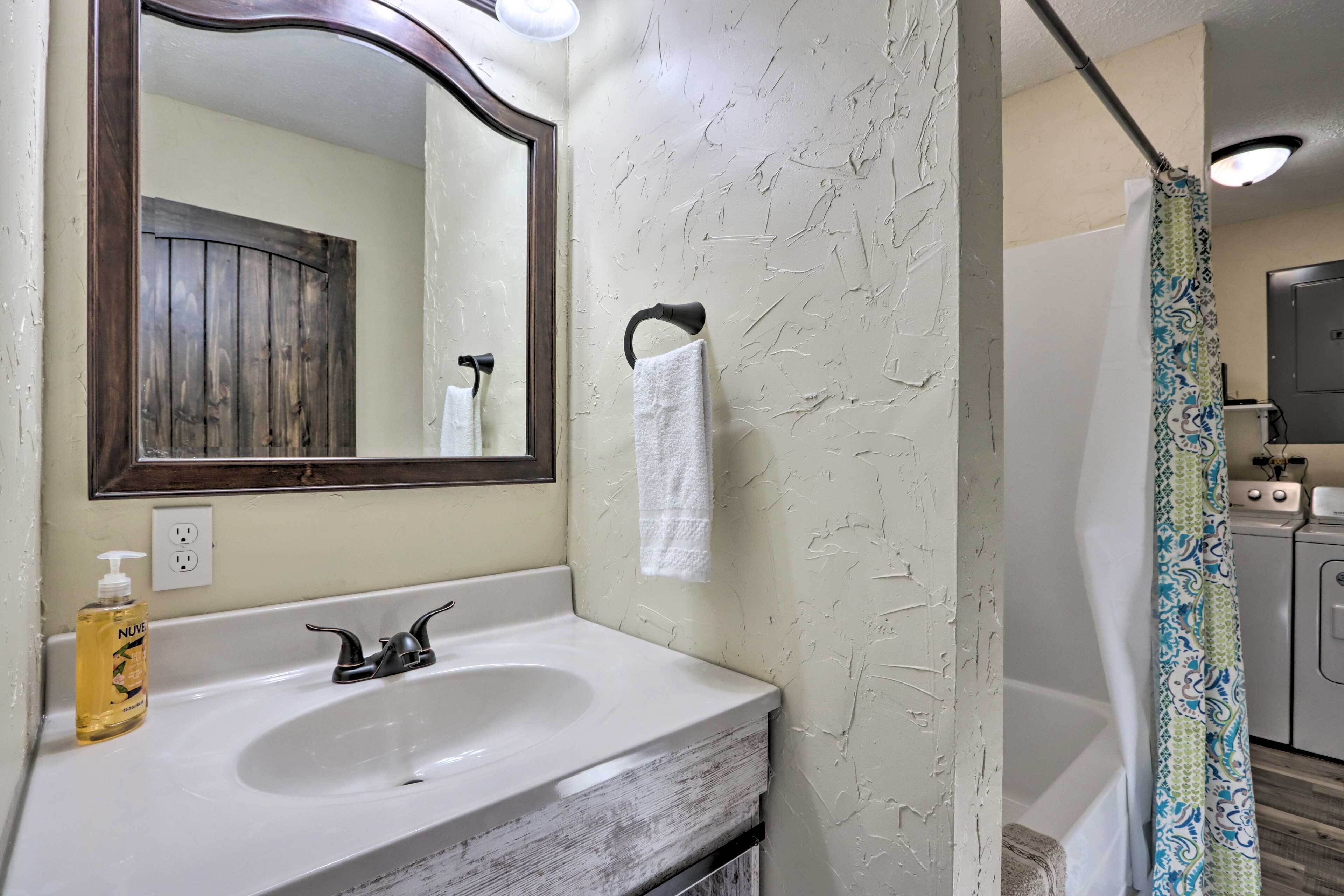 A bathroom with a white sink, a mirror, a towel hanging on a hook, a shower curtain, and a washing machine.