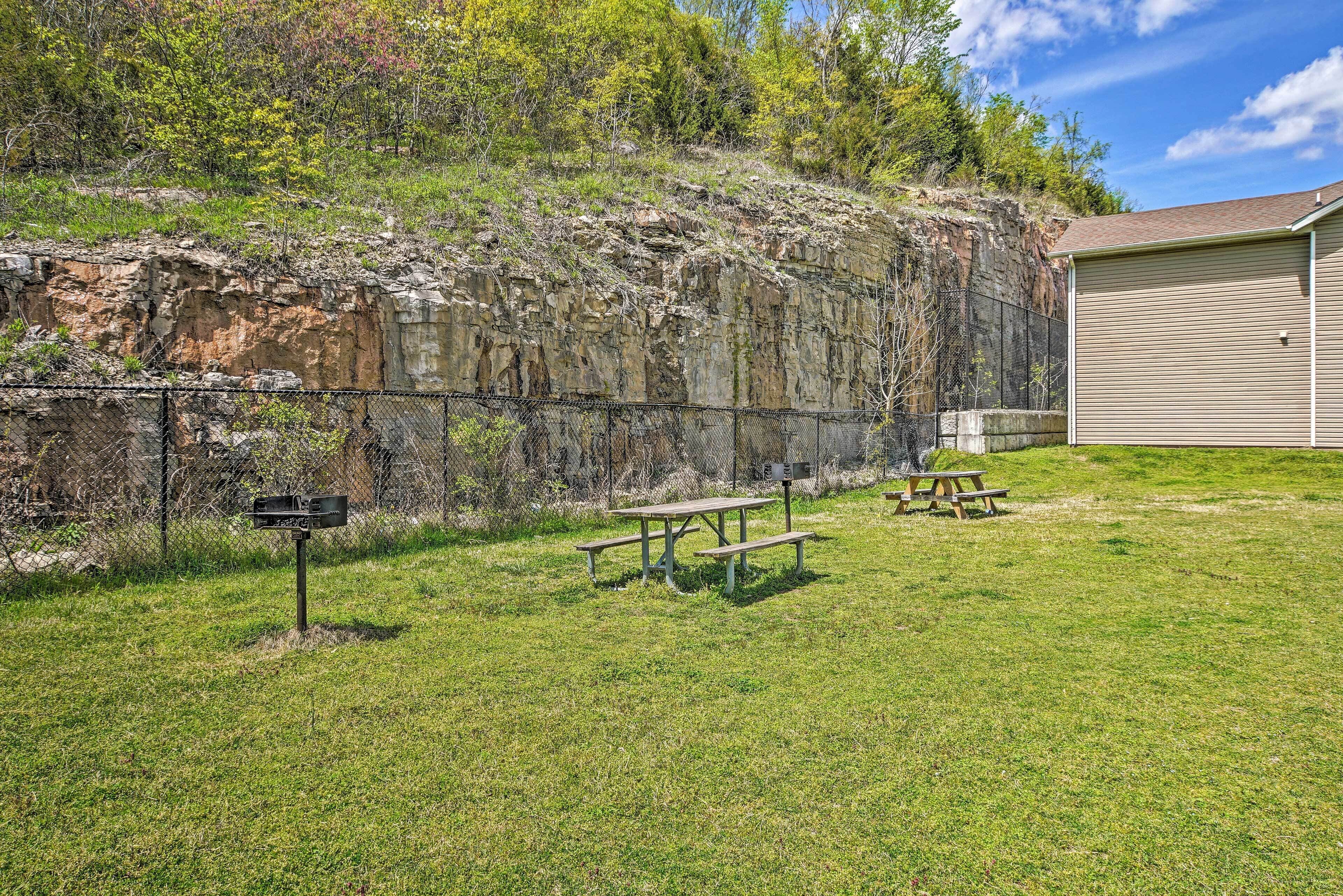 A picnic area with benches and a mailbox, surrounded by a grassy field and a rocky cliff.