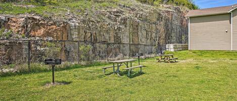 A picnic area with benches and a mailbox, surrounded by a grassy field and a rocky cliff.