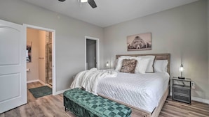Une chambre à coucher comprenant un lit, un banc, une table de chevet, un ventilateur de plafond et une porte donnant sur une autre pièce.