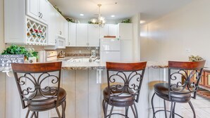 A kitchen with white cabinets, a central island with bar stools, and a chandelier.