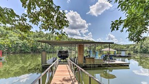 A wooden dock leading to a covered area with a boat and seating. - Lakefront Family Retreat in Osage Beach! (Osage Beach)