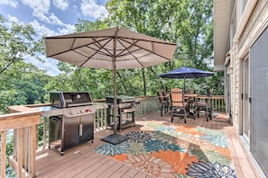 An outdoor deck with a grill, chairs, and a large umbrella.