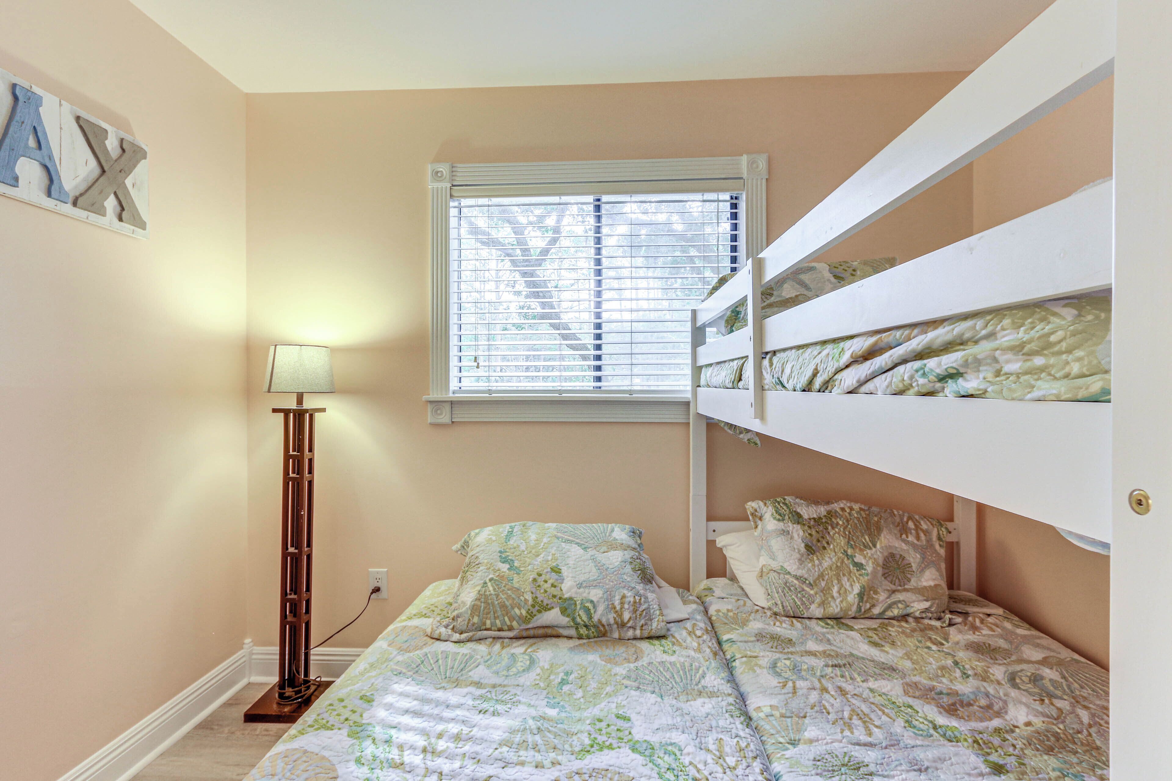 A bedroom with bunk beds, a bedside lamp, a window with blinds, and a wall-mounted light switch.