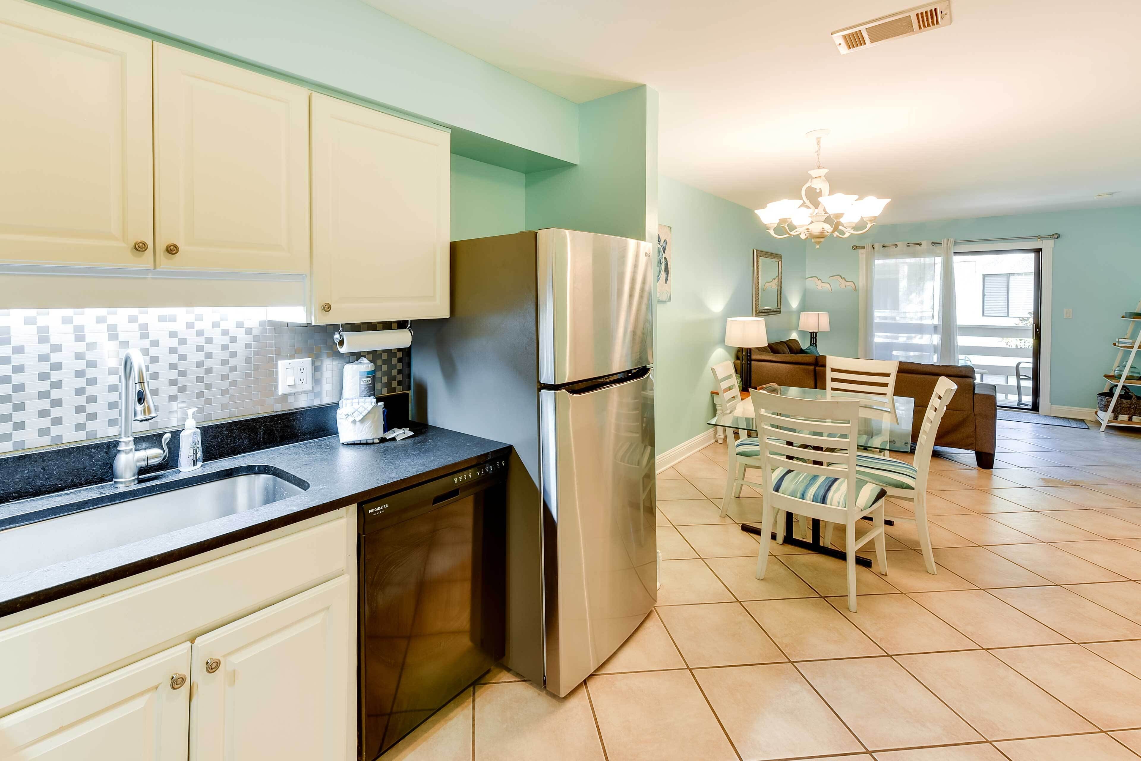 A kitchen with white cabinets, a stainless steel refrigerator, and a dishwasher. There is a dining area with a table and chairs.