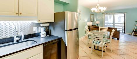 A kitchen with white cabinets, a stainless steel refrigerator, and a dishwasher. There is a dining area with a table and chairs.