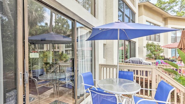 A glass-enclosed patio with a round table and blue chairs, a blue umbrella, and a wooden deck. - Patio & Walk to Beach: Hilton Head Island Townhome (Hilton Head Island)