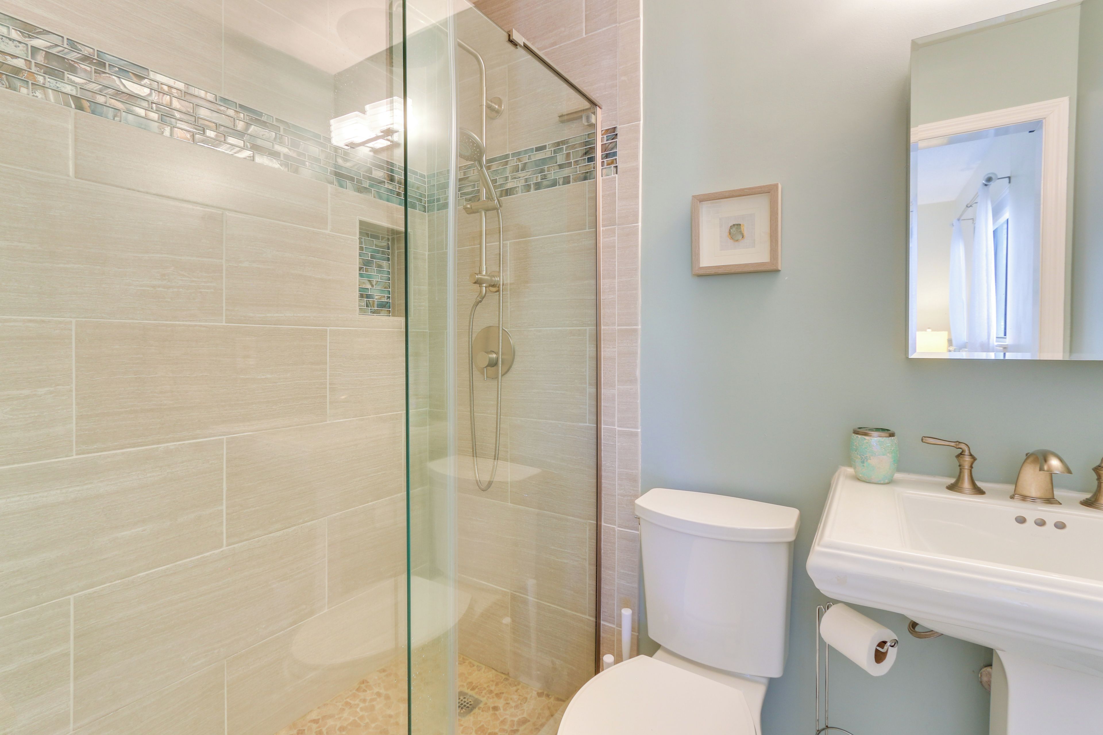 A bathroom with a glass-enclosed shower, a white toilet, and a sink with a mirror above it.