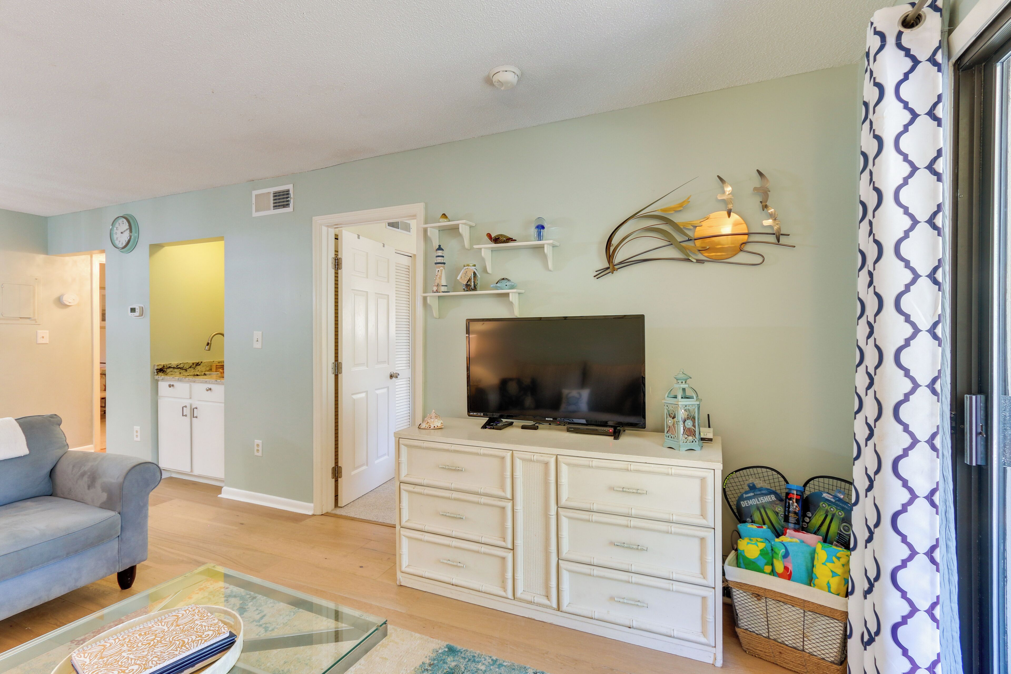 A living room with a sofa, TV, white cabinets, and a decorative wall piece.