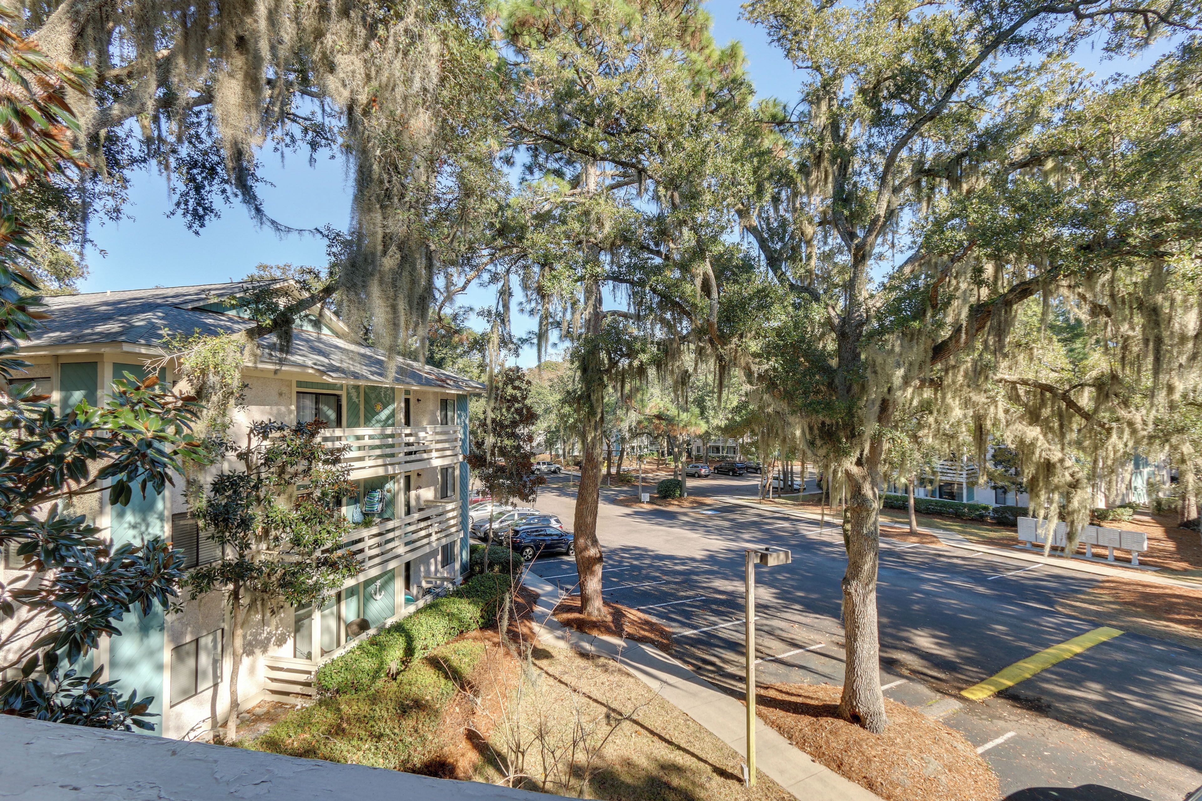 A residential street with a two-story house, a sidewalk, and trees with Spanish moss.