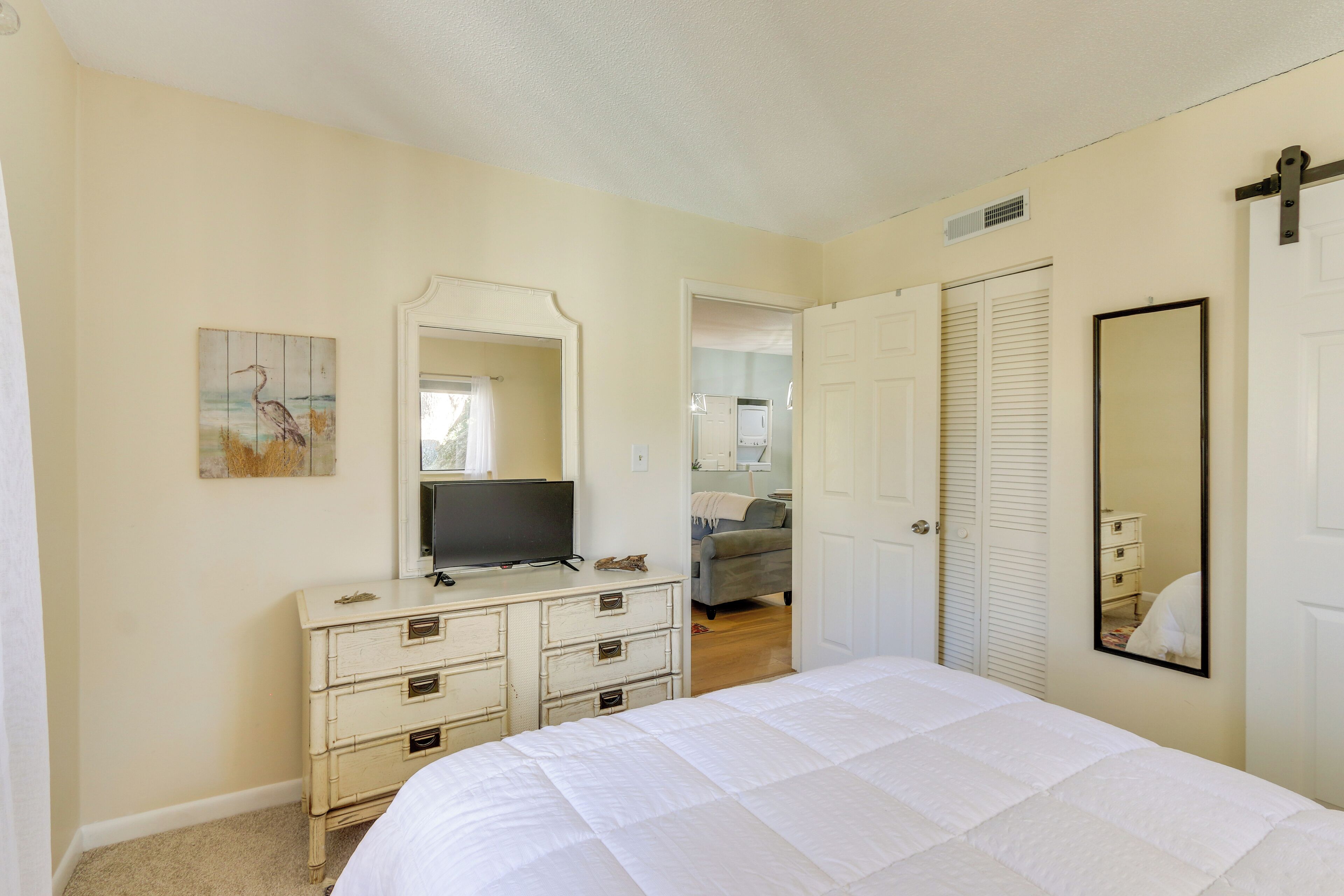 A bedroom with a bed, dresser, television, and a door leading to another room.