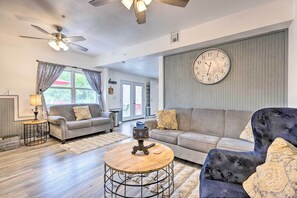A living room with a grey sofa, a round coffee table, a wall clock, and a ceiling fan. - 'hilltop Hideaway' Branson Home w/ Trampoline! (Branson)