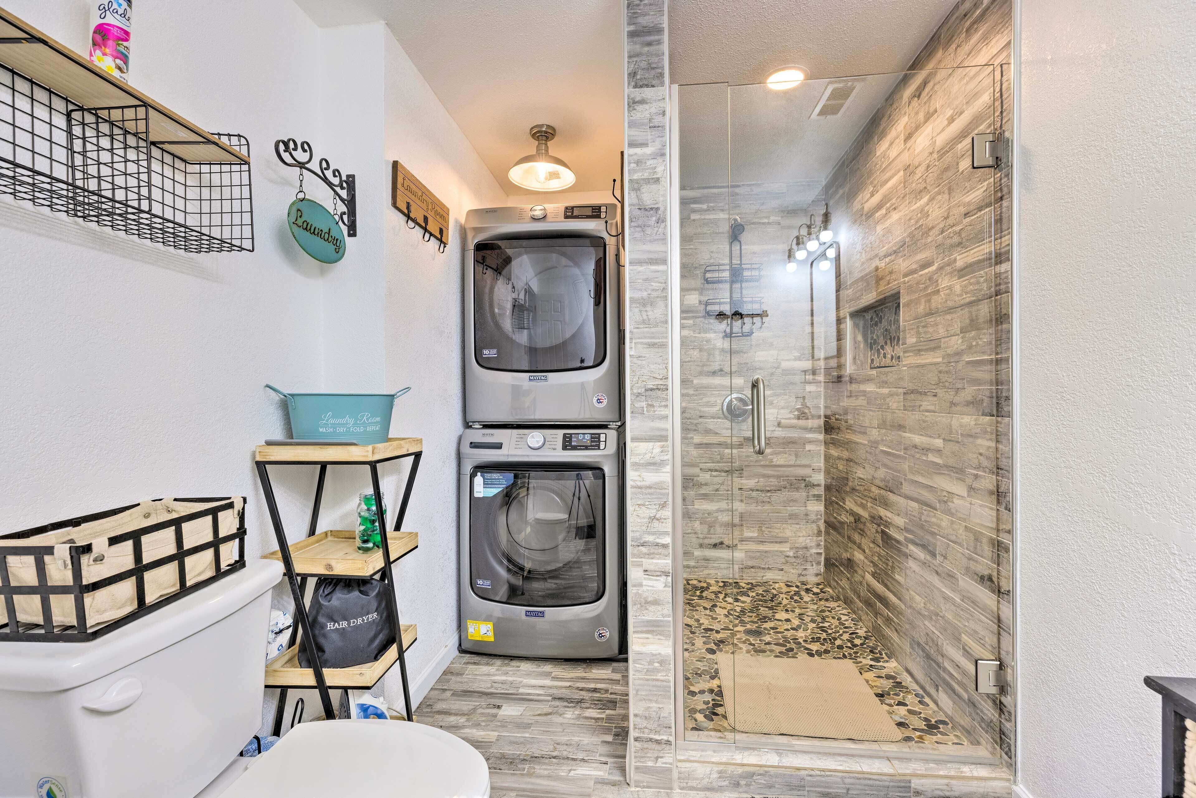 A compact bathroom with a shower, two stacked washers, and a small laundry station.