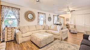 Ein geräumiges Wohnzimmer mit Ecksofa, Ottoman und Deckenventilator.