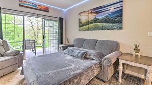 Un dormitorio con una cama grande, un sofá gris, una mesita con una planta y un cuadro en la pared.