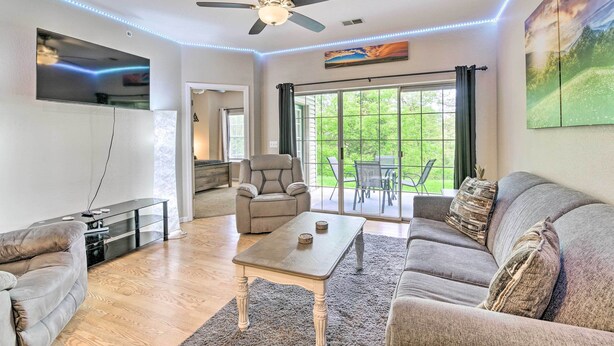 Una sala de estar moderna con ventilador de techo, televisor de pantalla plana y ventanas amplias.