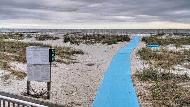 A beach path with a blue mat leading to the ocean, a signboard with information, and a railing. - Walk to Folly Field Beach: Hilton Head Condo (Hilton Head Island)