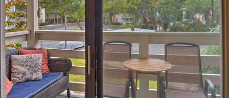 Un espace extérieur aménagé, abrité et doté d'un canapé en osier et d'une petite table, offrant une vue sur la rue et la verdure.