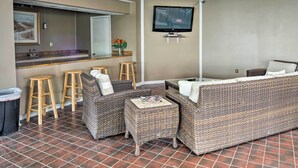 A living area with wicker furniture, a bar counter, stools, and a television mounted on the wall. - Walk to Folly Field Beach: Hilton Head Condo (Hilton Head Island)